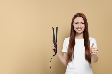 Photo of Beautiful woman with hair iron showing thumbs up on beige background, space for text