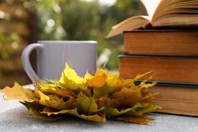 Yellow maple leaves, books and cup of tea on light gray table, closeup. Autumn atmosphere