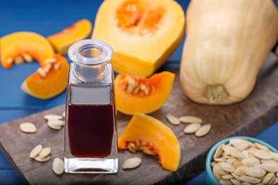 Photo of Fresh pumpkin seed oil in glass bottle on blue wooden table