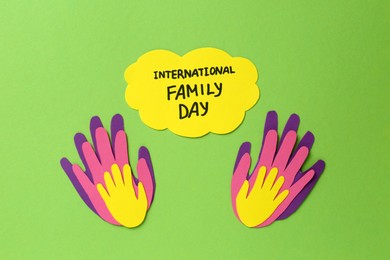 Paper palms and card with text International Family Day on light green background, flat lay