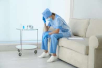 Exhausted doctor sitting on sofa indoors, blurred view. Stress of health care workers during COVID-19 pandemic