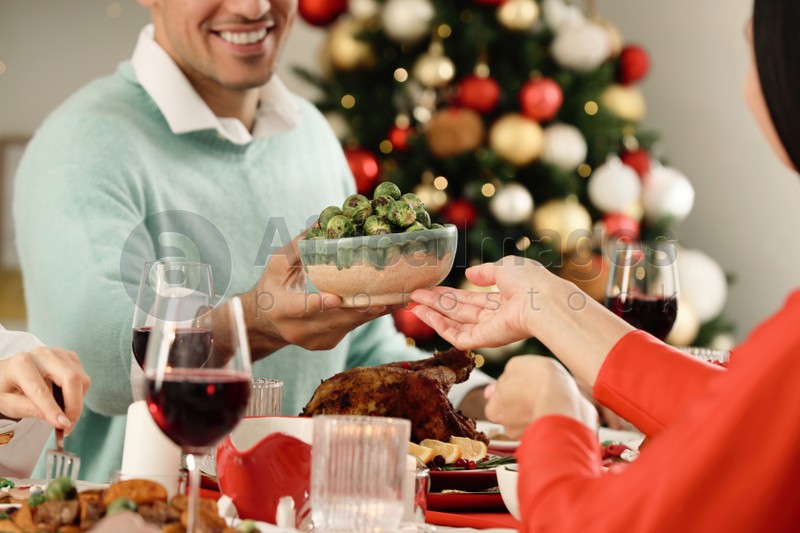 Photo of Man giving bowl with Brussels sprouts to woman at festive dinner indoors, closeup. Christmas Eve celebration