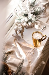Golden cup of cocoa and Christmas decor on window sill indoors