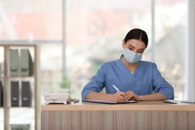 Receptionist with protective mask working at countertop in hospital