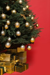 Beautifully decorated Christmas tree and many gift boxes on red background, closeup