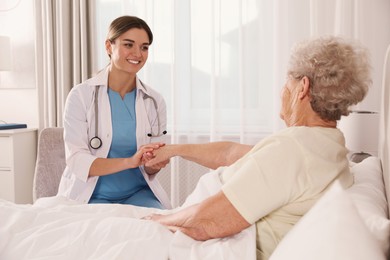 Young caregiver talking to senior woman in bedroom. Home health care service