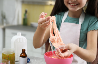 Little girl kneading DIY slime toy at table in kitchen, closeup