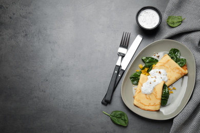 Delicious thin pancakes with spinach and sour cream on grey table, flat lay. Space for text