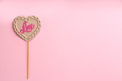 Chocolate heart shaped lollipop with word Love on light pink background, top view. Space for text