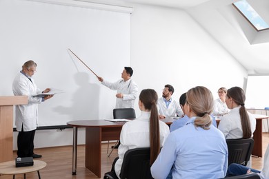 Photo of Doctors giving lecture near projection screen in conference room