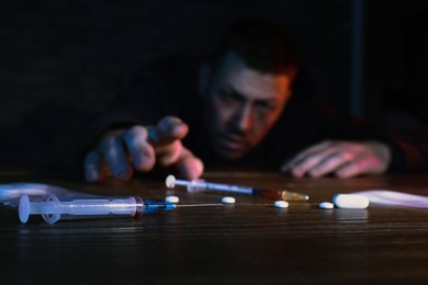 Addicted man reaching to drugs at table, focus on syringe