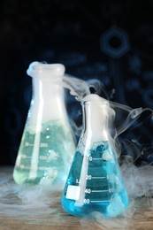 Photo of Laboratory glassware with colorful liquids and steam on wooden table against black background, space for text. Chemical reaction