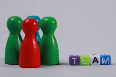 Colorful pawns and cubes with word Team on light grey background, closeup. Recruiter searching employee