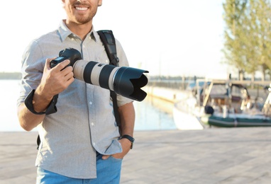 Young male photographer holding professional camera at pier. Space for text