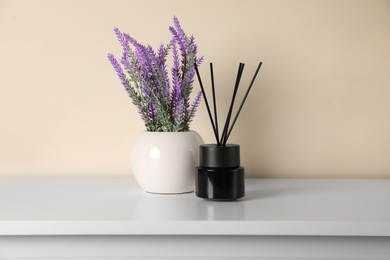 Photo of Aromatic reed air freshener and lavender flowers on white table indoors