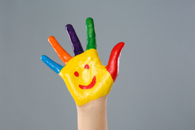 Kid with smiling face drawn on palm against grey background, closeup