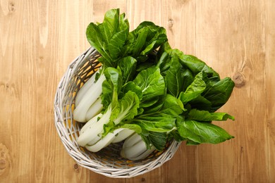 Fresh green pak choy cabbages in wicker basket on wooden table, top view