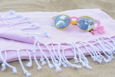 Photo of Blanket with stylish sunglasses and flower on sand outdoors, closeup. Beach accessories