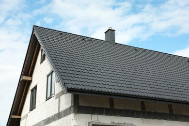 Unfinished house with grey roof against cloudy sky, low angle view