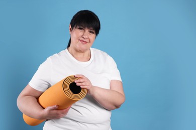 Happy overweight mature woman with yoga mat on light blue background. Space for text