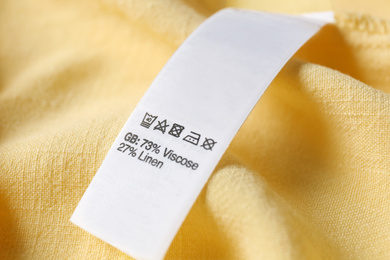 Clothing label with care symbols and material content on yellow shirt, closeup view