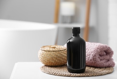 Bottle of bubble bath, towel and wicker box on white table in bathroom, space for text