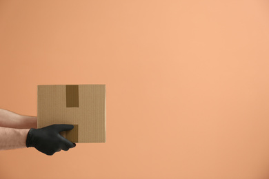 Courier holding cardboard box on orange background, space for text. Parcel delivery