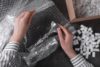 Photo of Woman covering silver candlesticks with bubble wrap at dark grey table, closeup