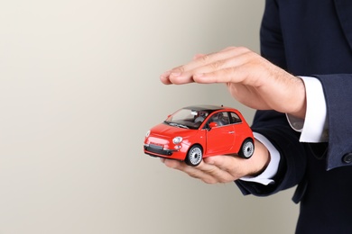 Male insurance agent holding toy car on light background, closeup. Space for text