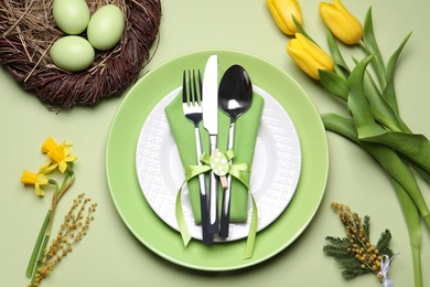 Festive Easter table setting with eggs on light green background, flat lay