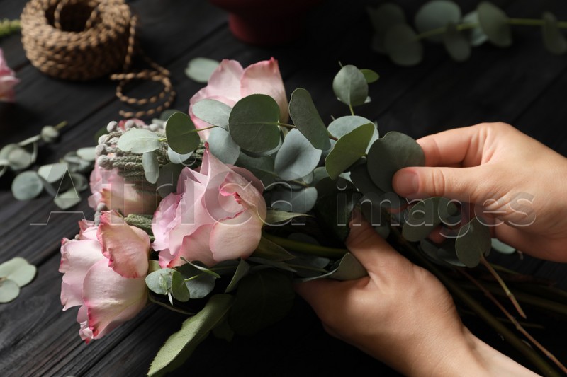 Florist creating beautiful bouquet at black wooden table, closeup