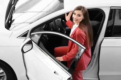 Young woman sitting in driver's seat of new car at salon