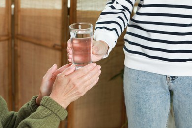 Caregiver giving water to elderly woman at home, closeup