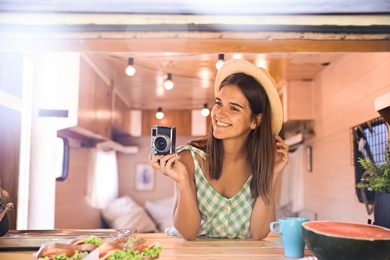 Young woman with vintage camera in trailer, view from outside. Camping vacation