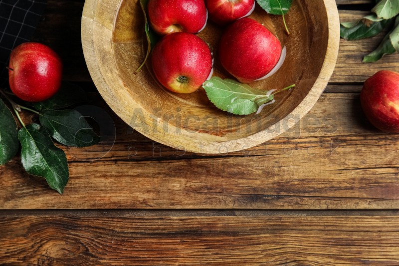 Photo of Ripe red apples in bowl of water on wooden table, flat lay. Space for text