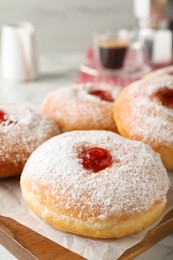 Delicious donuts with jam and powdered sugar on wooden board, closeup