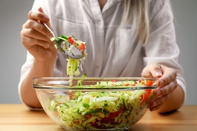 Woman making tasty salad with Chinese cabbage at wooden table, closeup