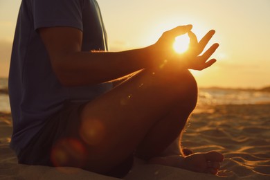 Man meditating on sandy beach at sunset, closeup