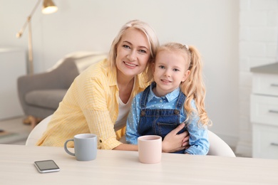 Portrait of mature woman and her granddaughter drinking tea at table indoors