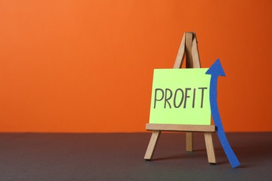 Economic profit. Easel with note and arrow on grey table against orange background, space for text