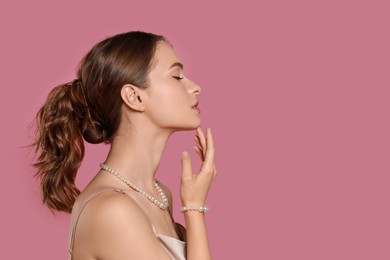 Young woman wearing elegant pearl jewelry on pink background, space for text