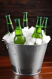 Photo of Metal bucket with bottles of beer and ice cubes on wooden table