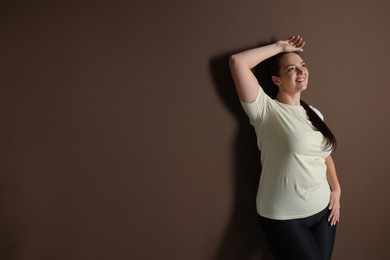 Happy overweight woman on brown background, space for text