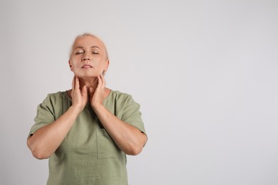 Mature woman doing thyroid self examination on light grey background, space for text