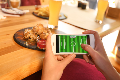 Woman playing game using smartphone at table with tasty BBQ wings in cafe, closeup