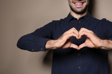 Photo of Man showing HEART gesture in sign language on color background, closeup