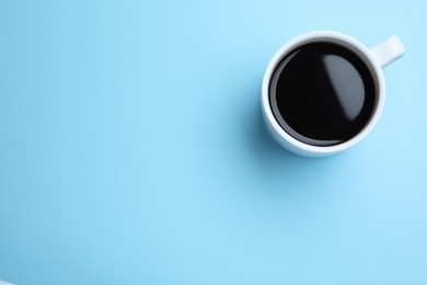 White mug of freshly brewed hot coffee on light blue background, top view. Space for text