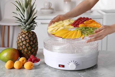 Woman putting tray with cut fruits into dehydrator machine at grey marble table in kitchen, closeup