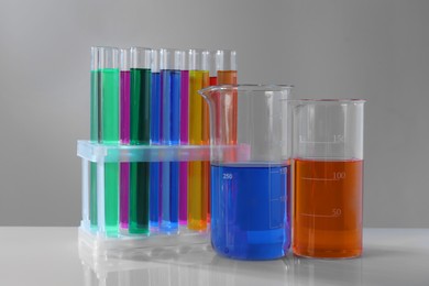 Photo of Different laboratory glassware with colorful liquids on white table against grey background