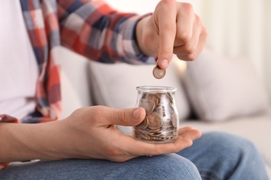 Man putting coin into glass jar at home, closeup